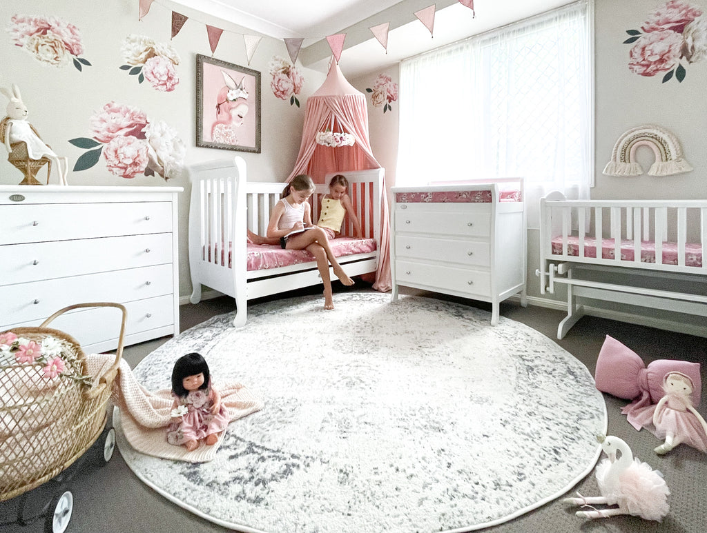Girls reading on sleigh cot in pink nursery with chest of drawers and change table and rocking cradle
